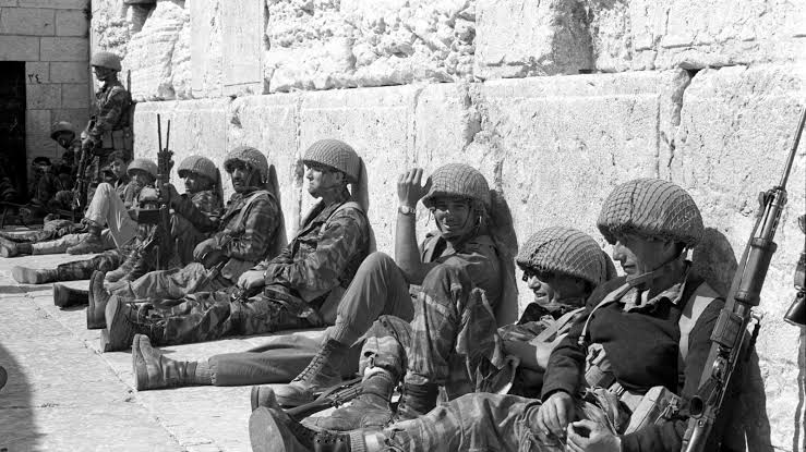 IMG-20260323-WA0002 Israeli soldiers resting during wartime near stone wall historical photo